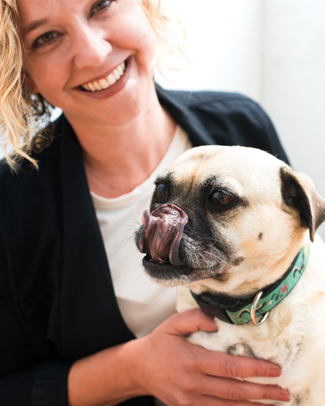 Woman smiling and holding a dog wearing a green collar.