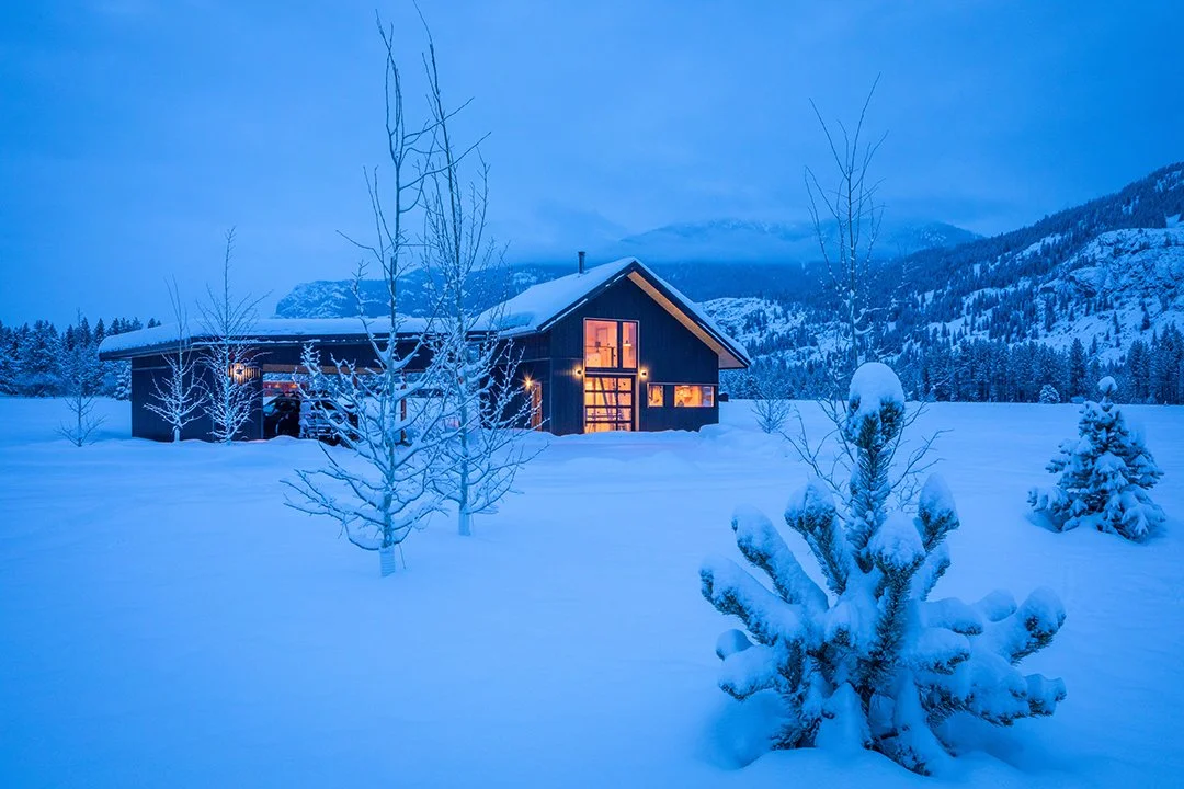 Small glowing house and a detached open garage in the middle of a snow covered valley.