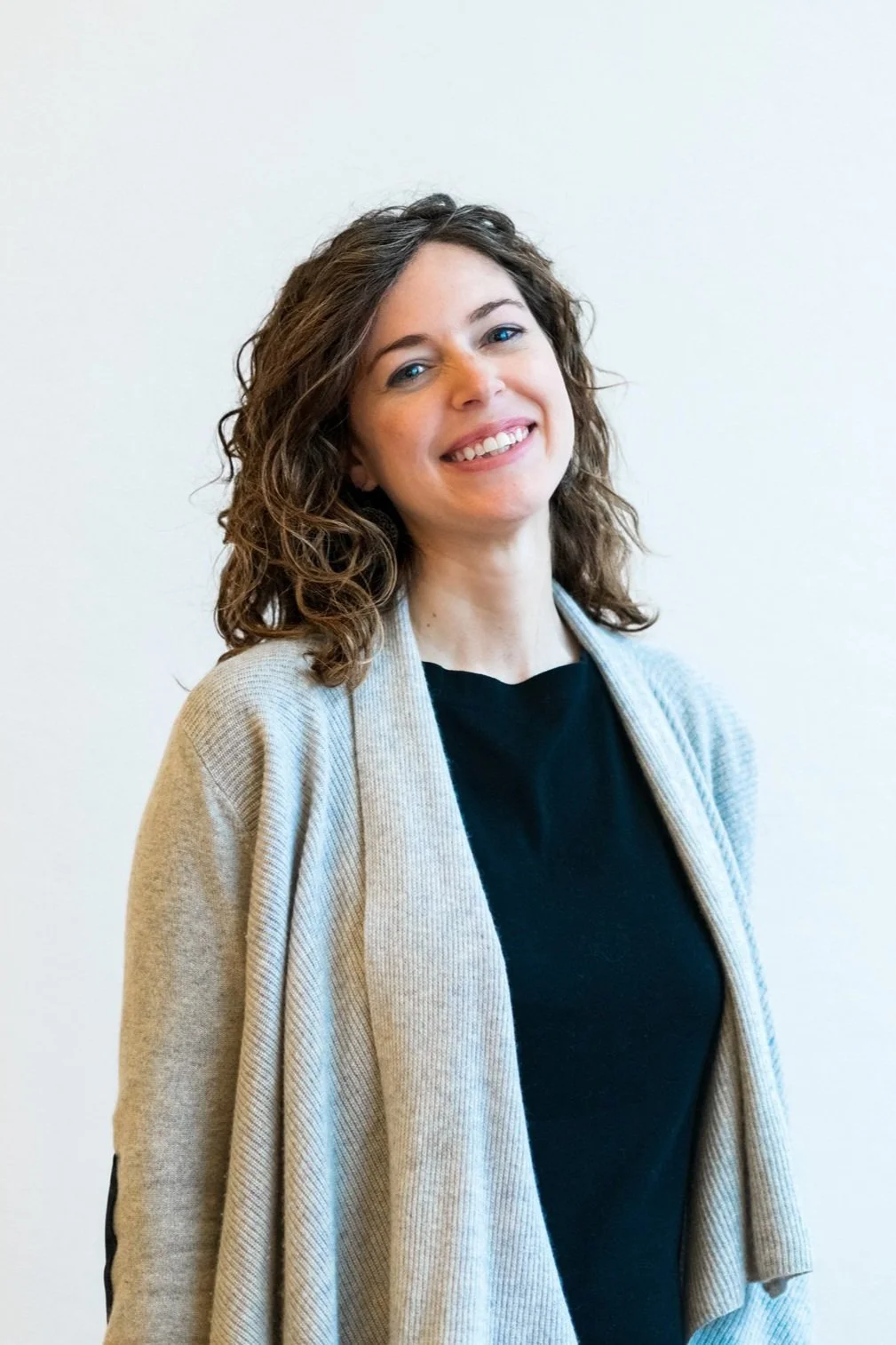 Smiling woman with curly hair wearing a gray sweater