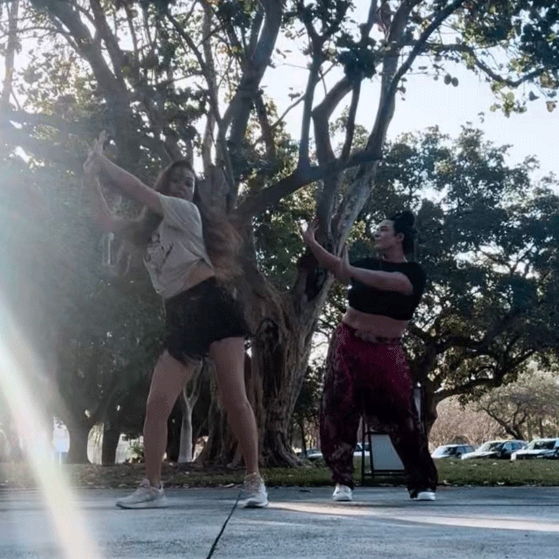 Two women dancing outdoors under a tree at Belly Heat class at George English Park in Fort Lauderdale
