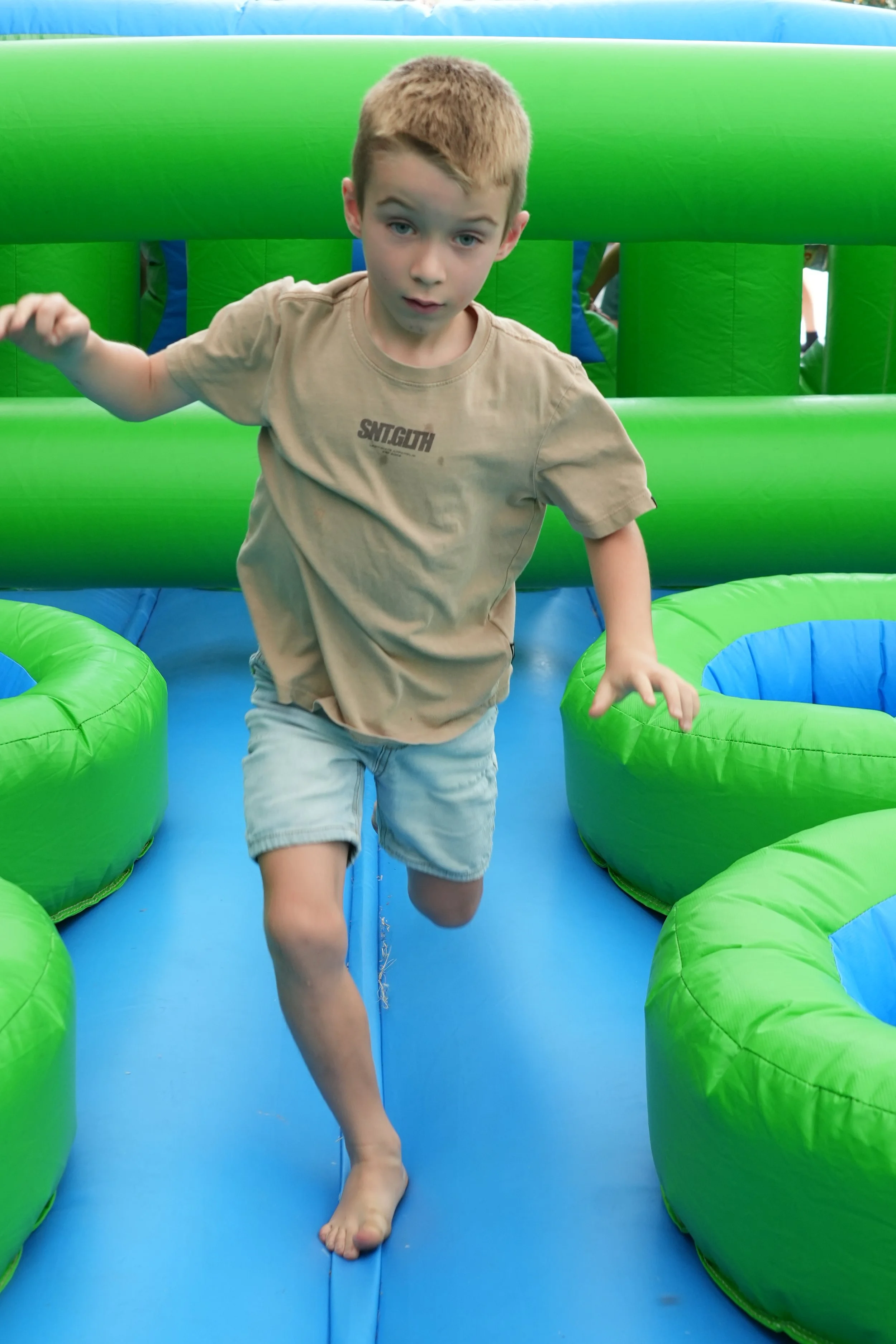 A boy running on an inflatable bounce house with green and blue sections.