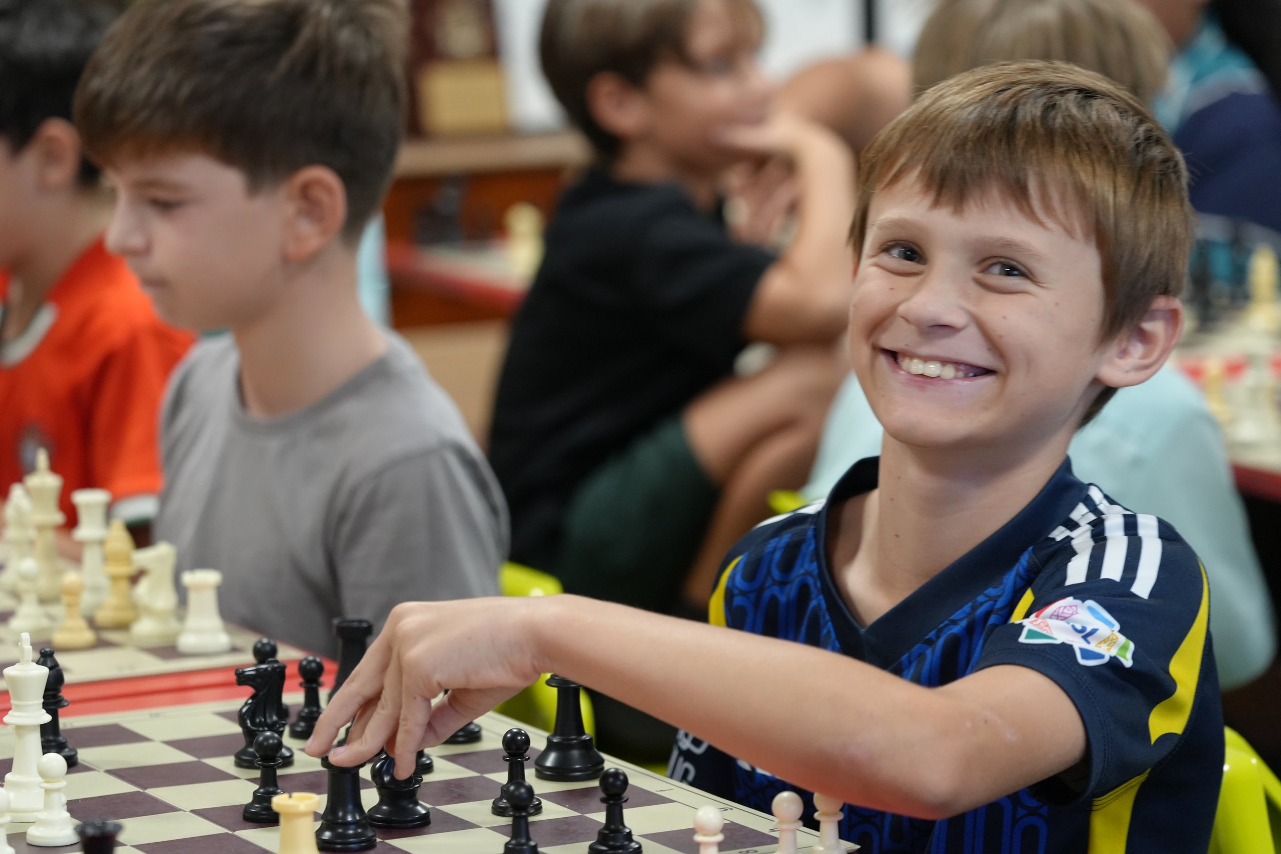 Young boy with glasses playing chess in a crowded classroom or chess club.