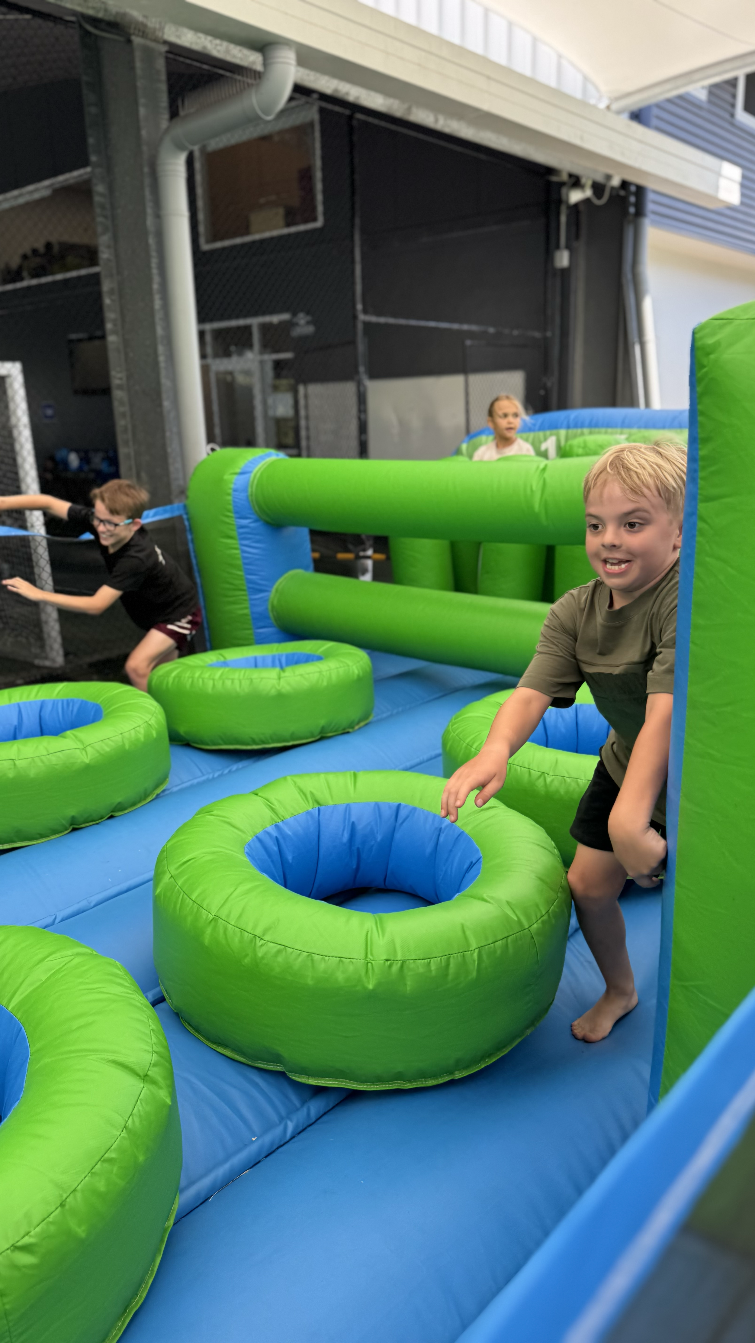 Children playing on a colorful inflatable obstacle course with green and blue sections, indoors.