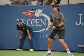 Tennis player preparing to serve at the US Open with a ballperson in the background.