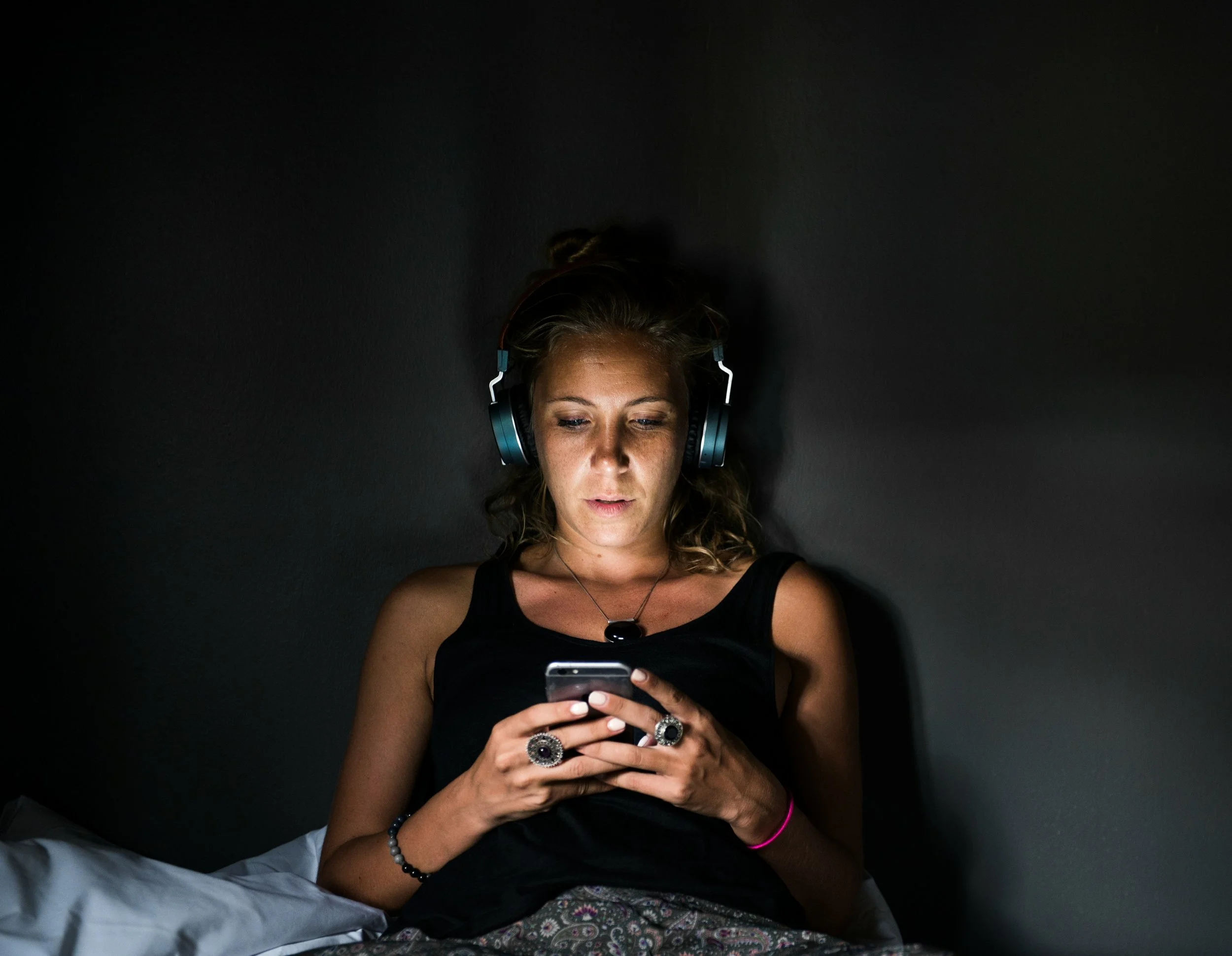 Woman scrolling on her phone in a dark room late at night, illustrating revenge bedtime procrastination and the urge to delay sleep.