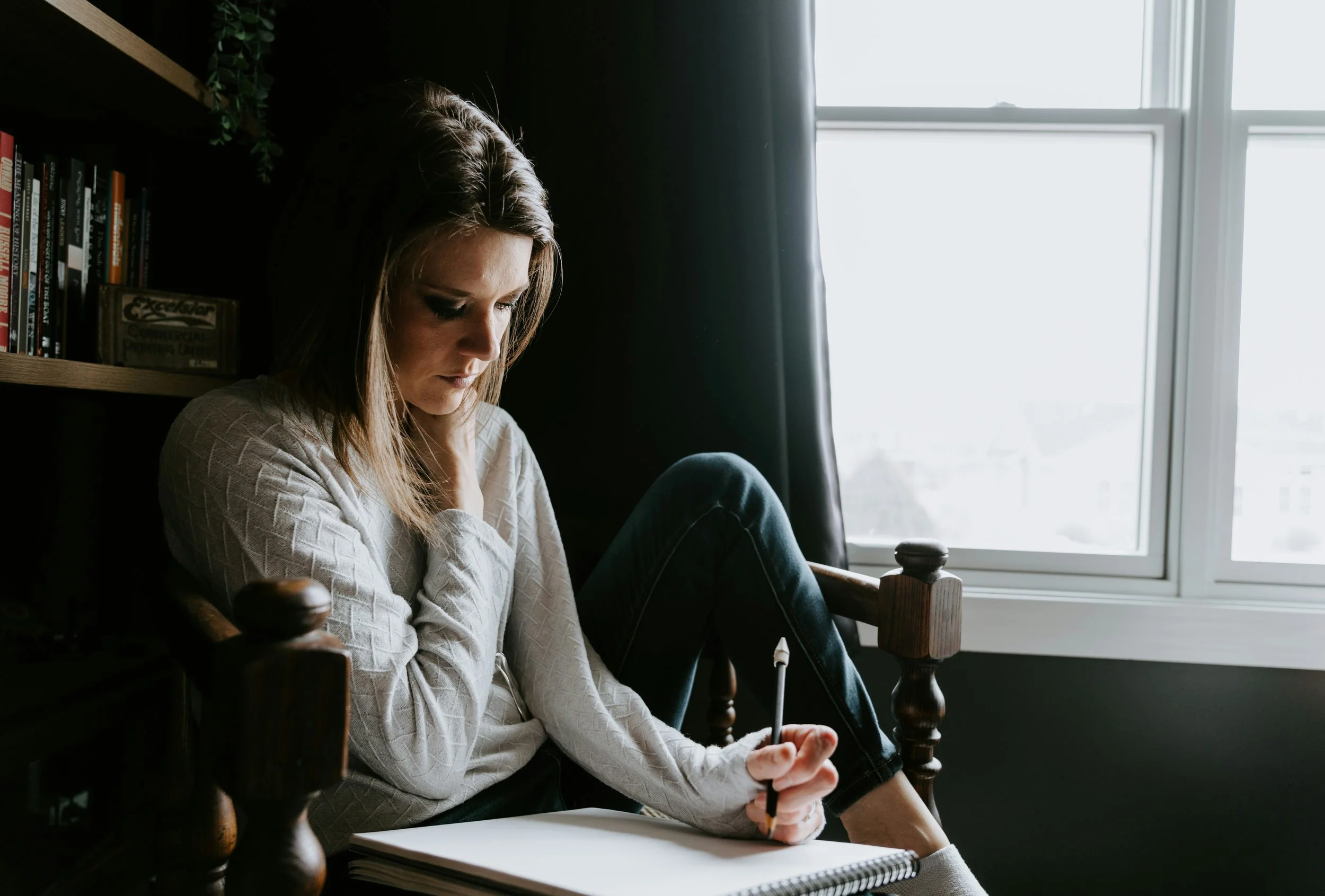 Woman journaling in a cozy chair by a window — practicing thought reframing exercises for mental health.
