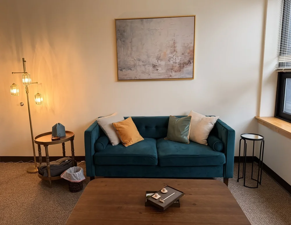 Therapy room at our Port Washington office, with a teal sofa and warm floor lamp