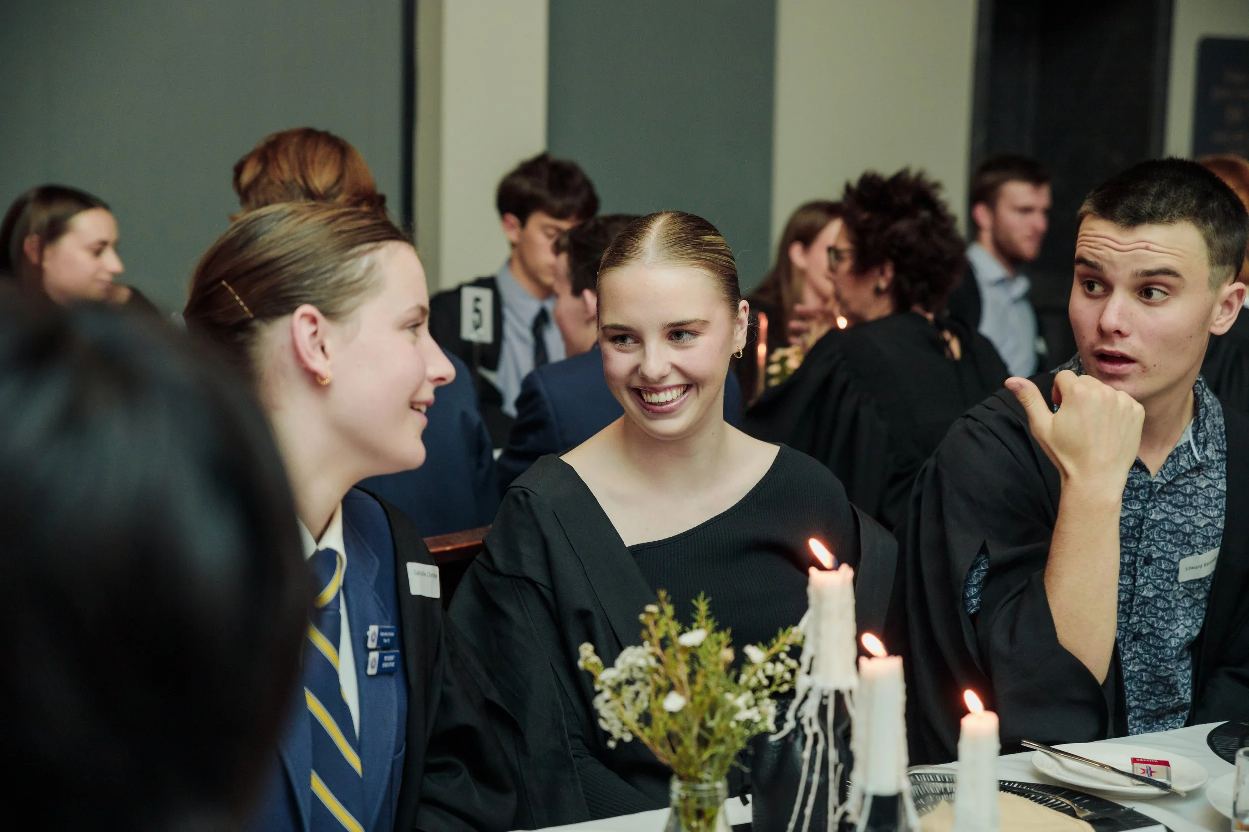 People dressed in formal attire celebrating at a dinner with candles and flowers on the table.