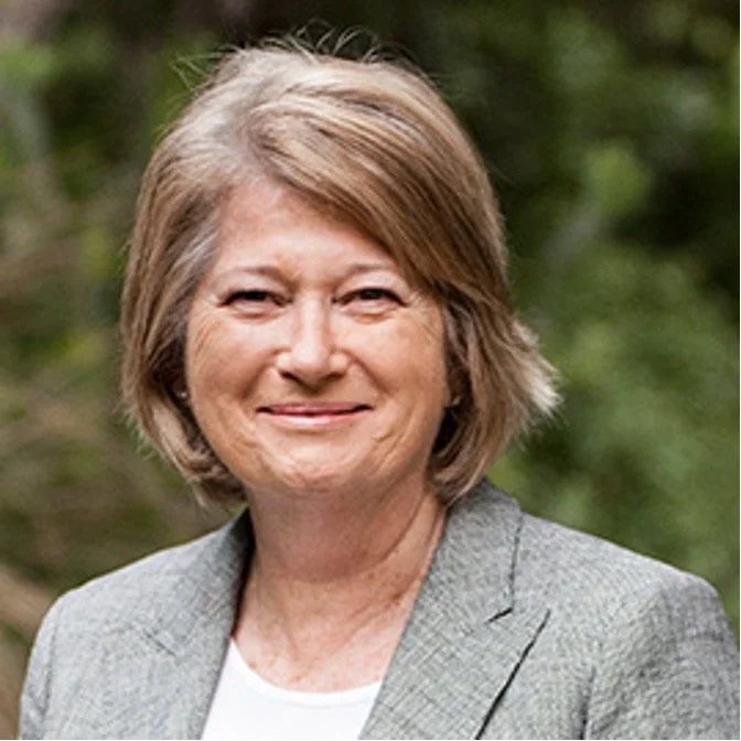 Portrait of a middle-aged woman with short blonde hair outdoors, wearing a gray blazer and white top, smiling