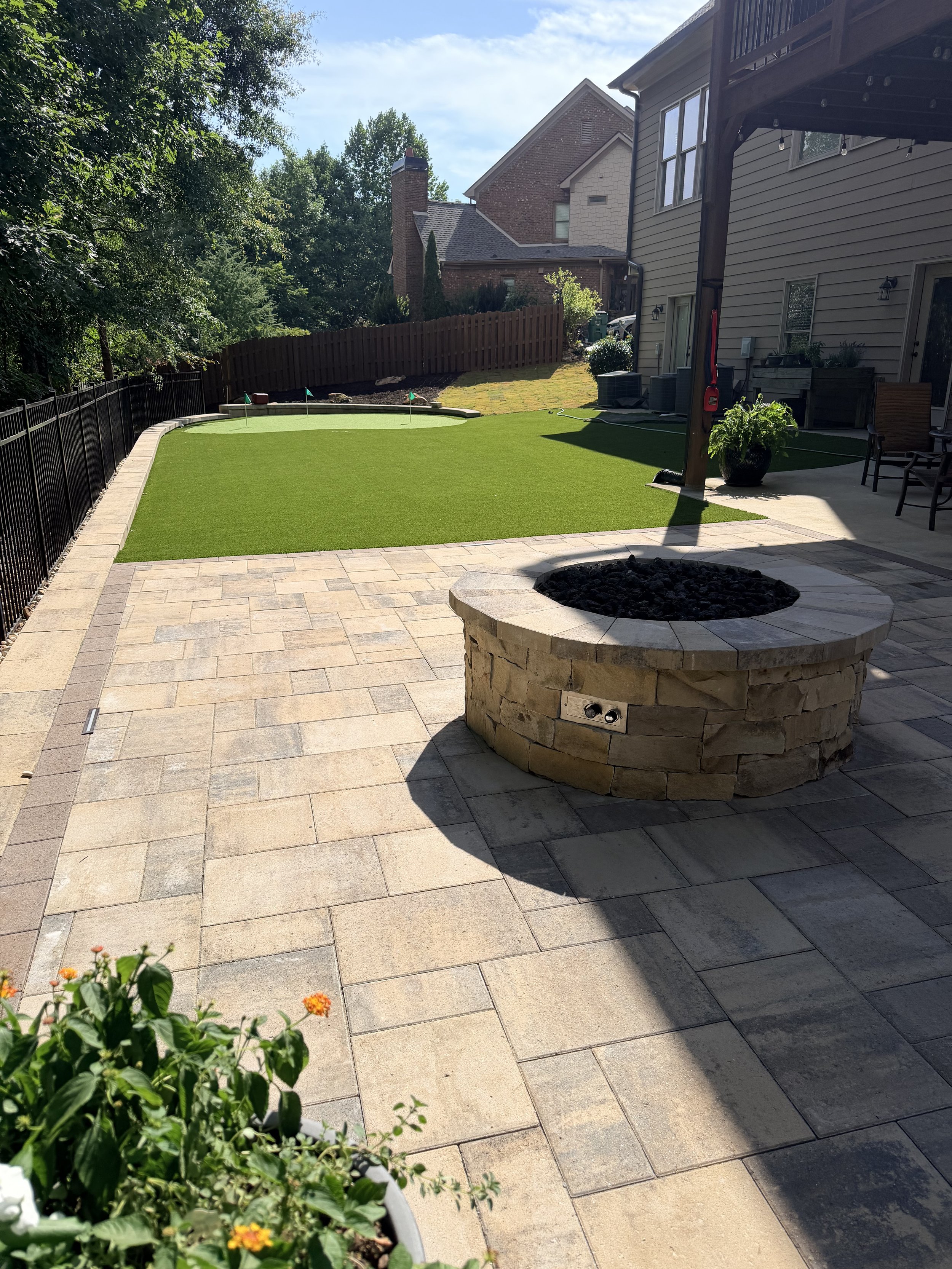 Backyard patio with a fire pit, potted plants, lawn, and a warehouse-style house in the background.