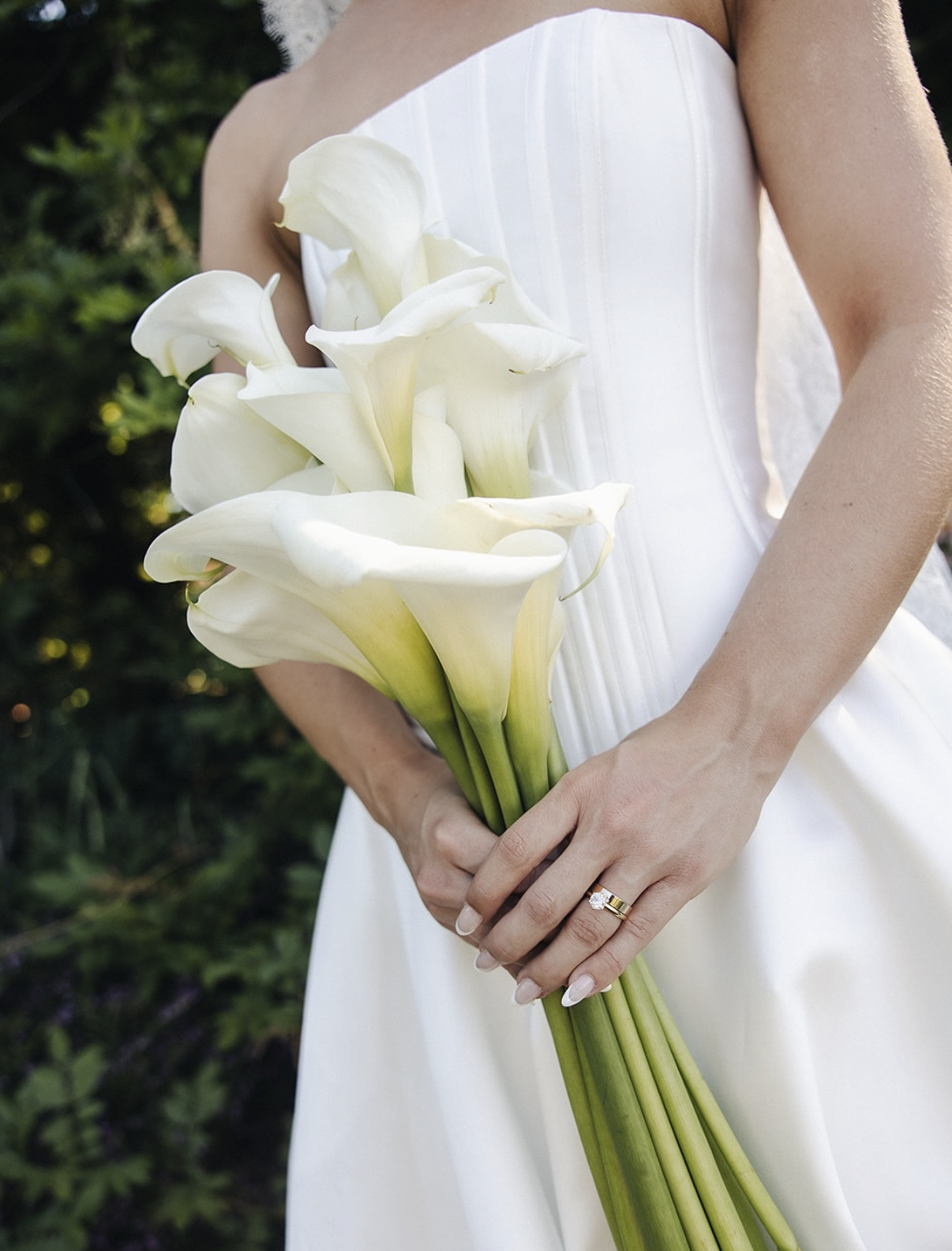 A woman in a white wedding dress holding a bouquet of white calla lilies.