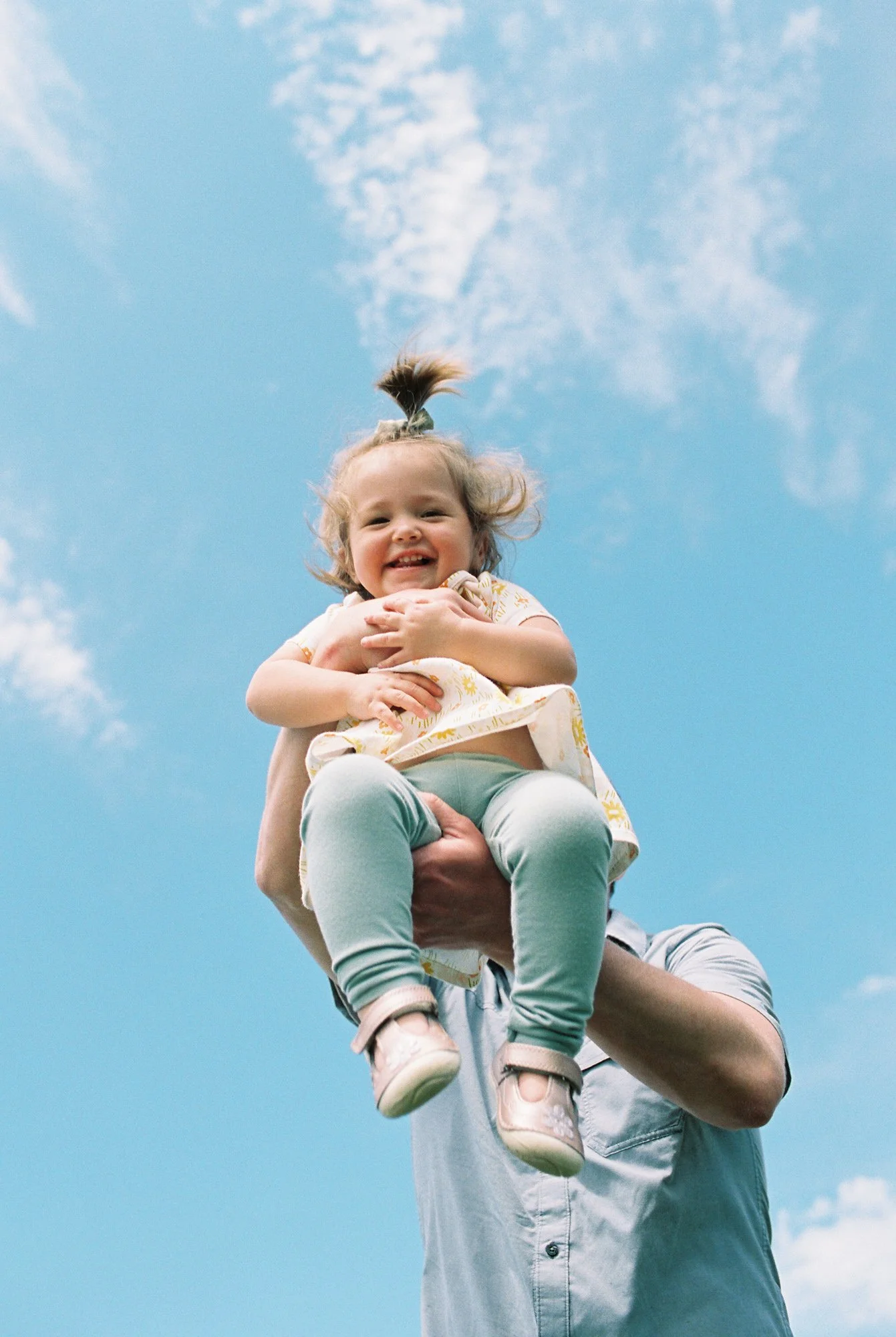 A father holding his daughter in the air against a bright blue sky; a lifestyle family photograph in Sioux Falls.