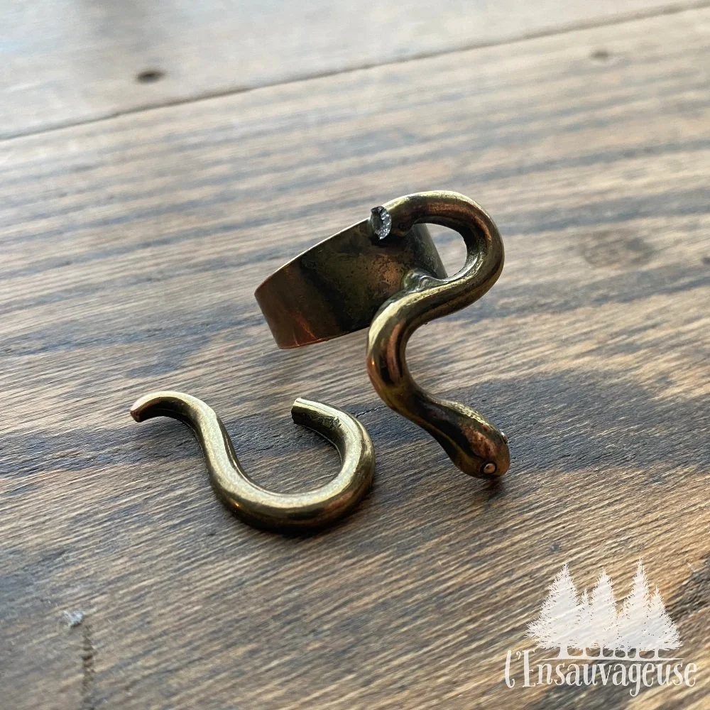 une bague en forme de serpent, brisée en deux. Sur une surface en bois.