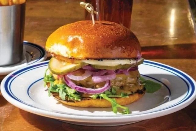 A burger with lettuce, pickles, onions, and a beef patty on a white plate and a wooden table.