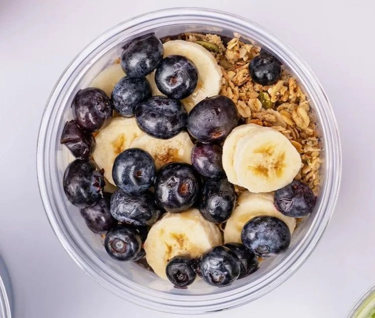 Top view of a clear bowl containing sliced bananas, blueberries, and granola.
