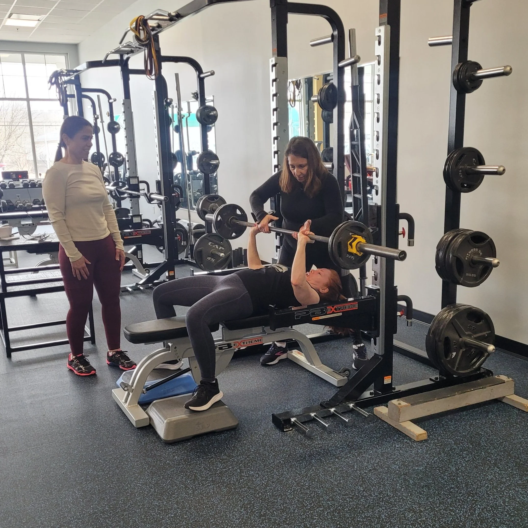 Personal Fitness Coach Debra Rydziel working with two women doing bench press and strength training. Our private gym allows for the best personal trainer experience.