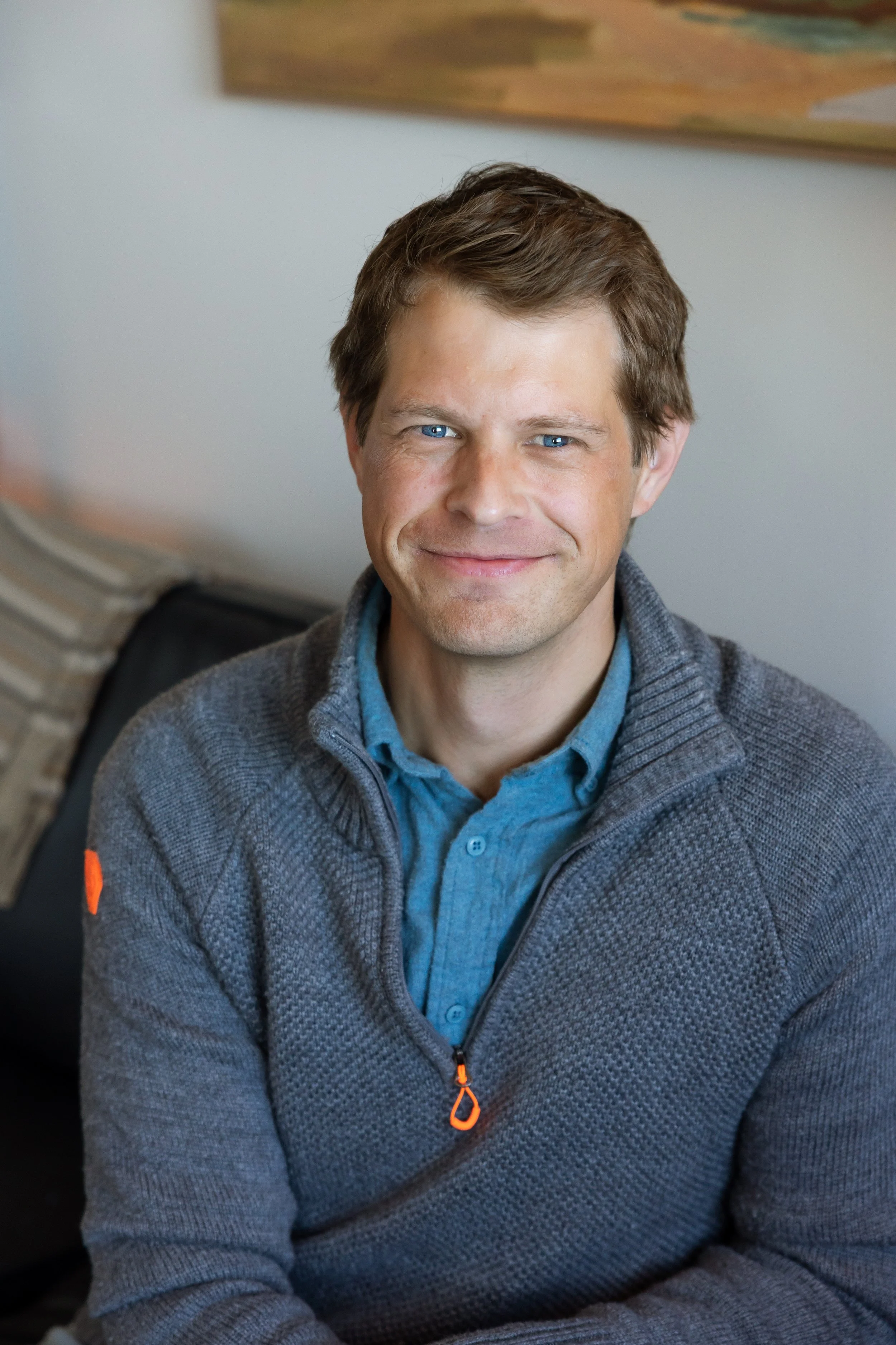 Grinning man in a blue 3/4 zip sweater.