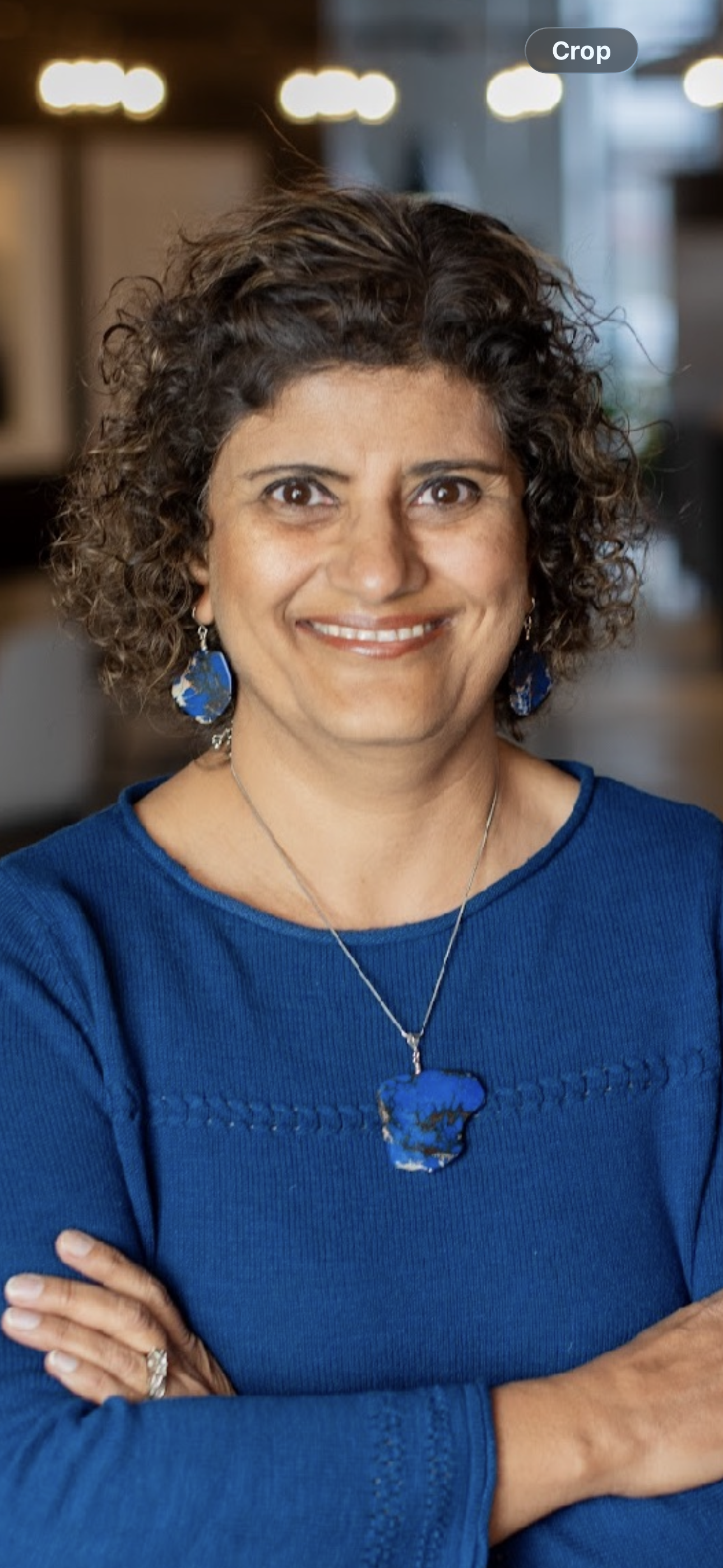 Woman with blue long sleeve top and short, brown curly hair.