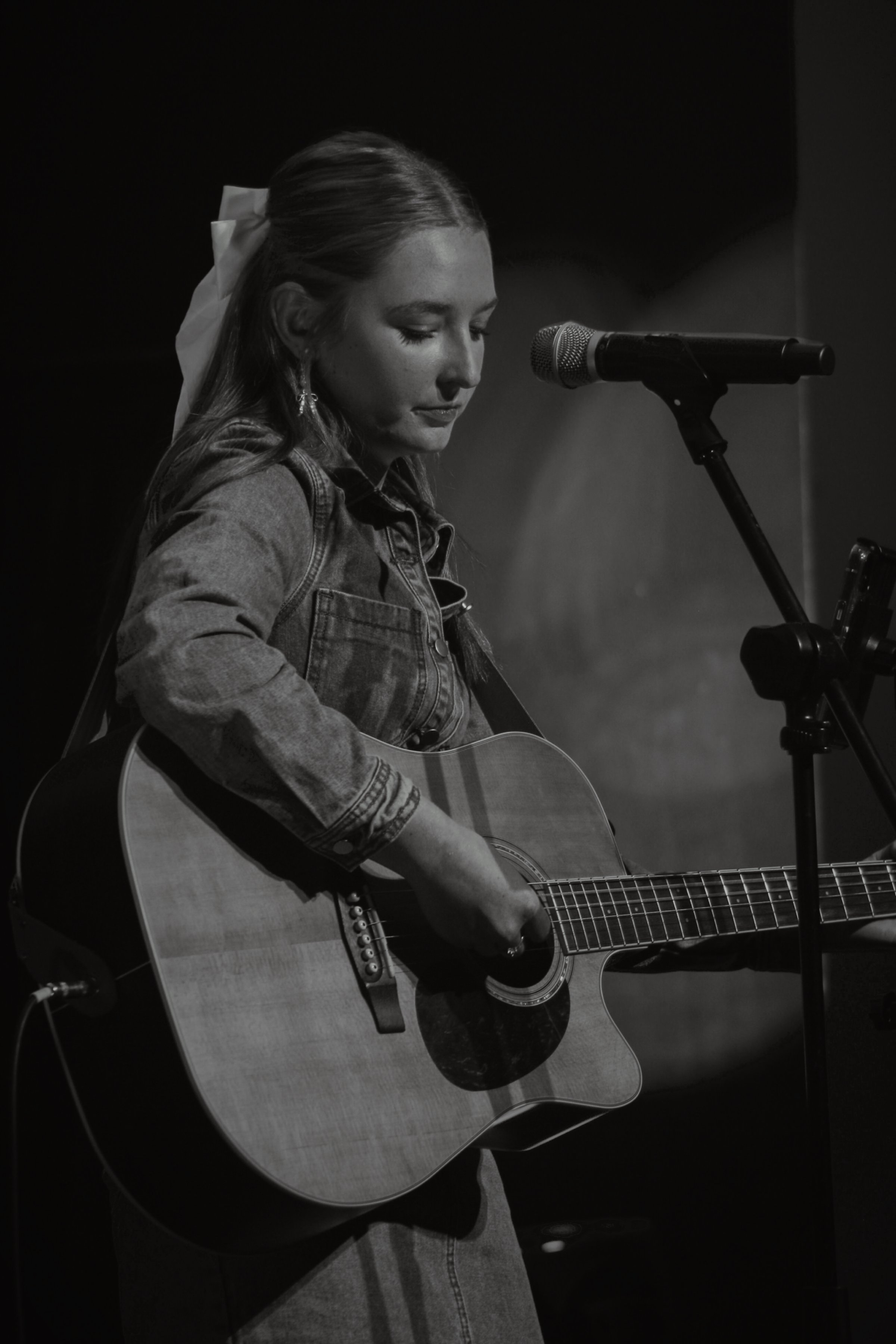 A woman playing an acoustic guitar on stage in black and white