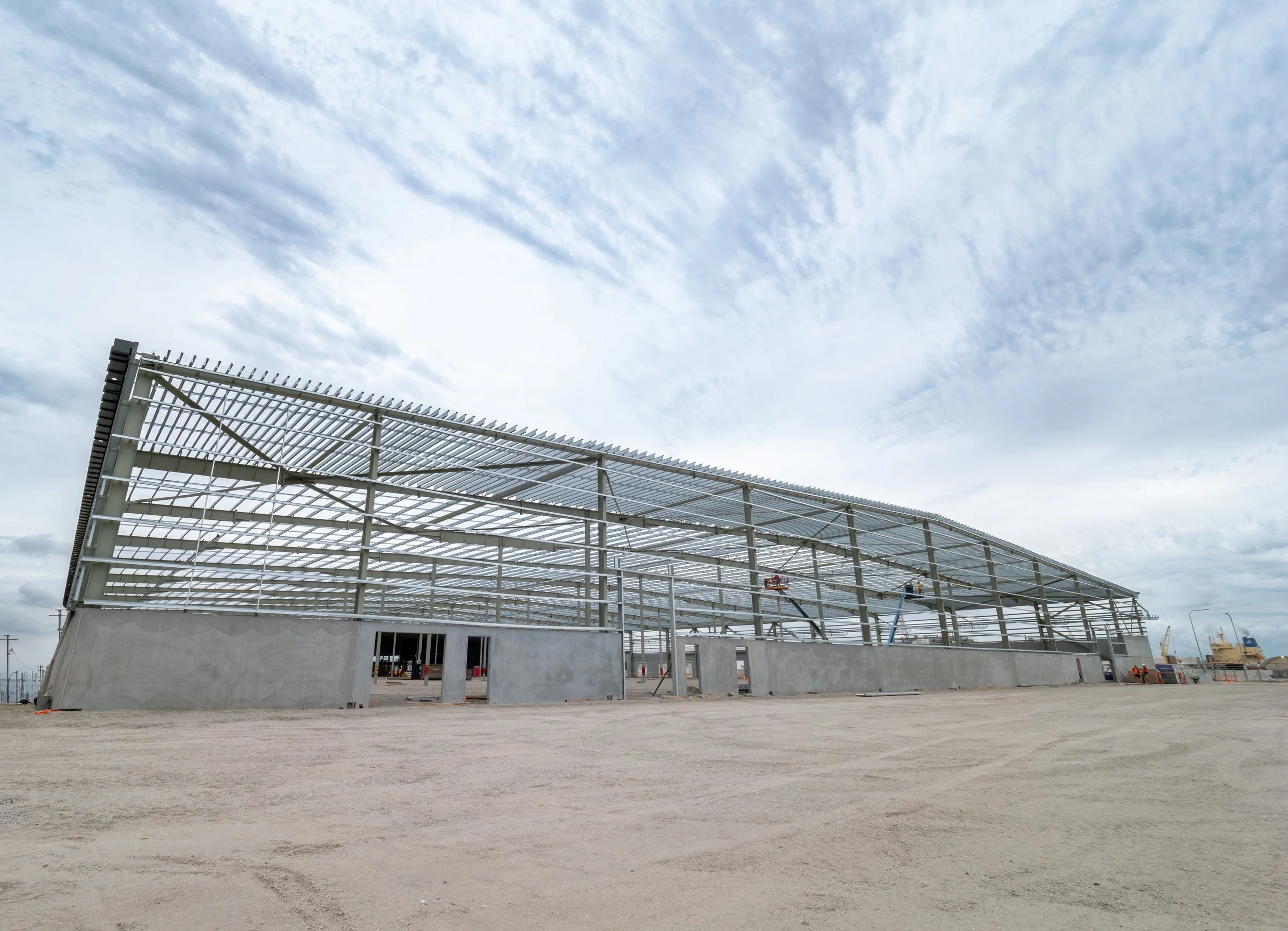 Steel framework of a building under construction with a cloudy sky in the background.