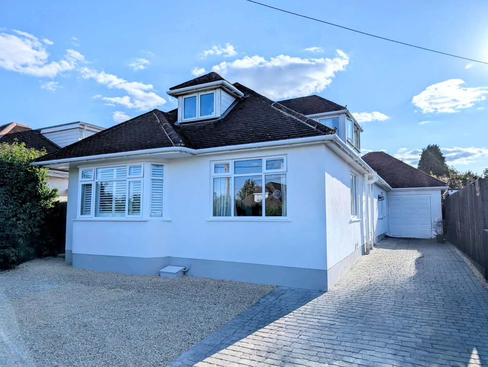 A modern two-story house with white walls, a sloped roof with shingles, a large window on the upper floor, and black gutters along the roof edges.