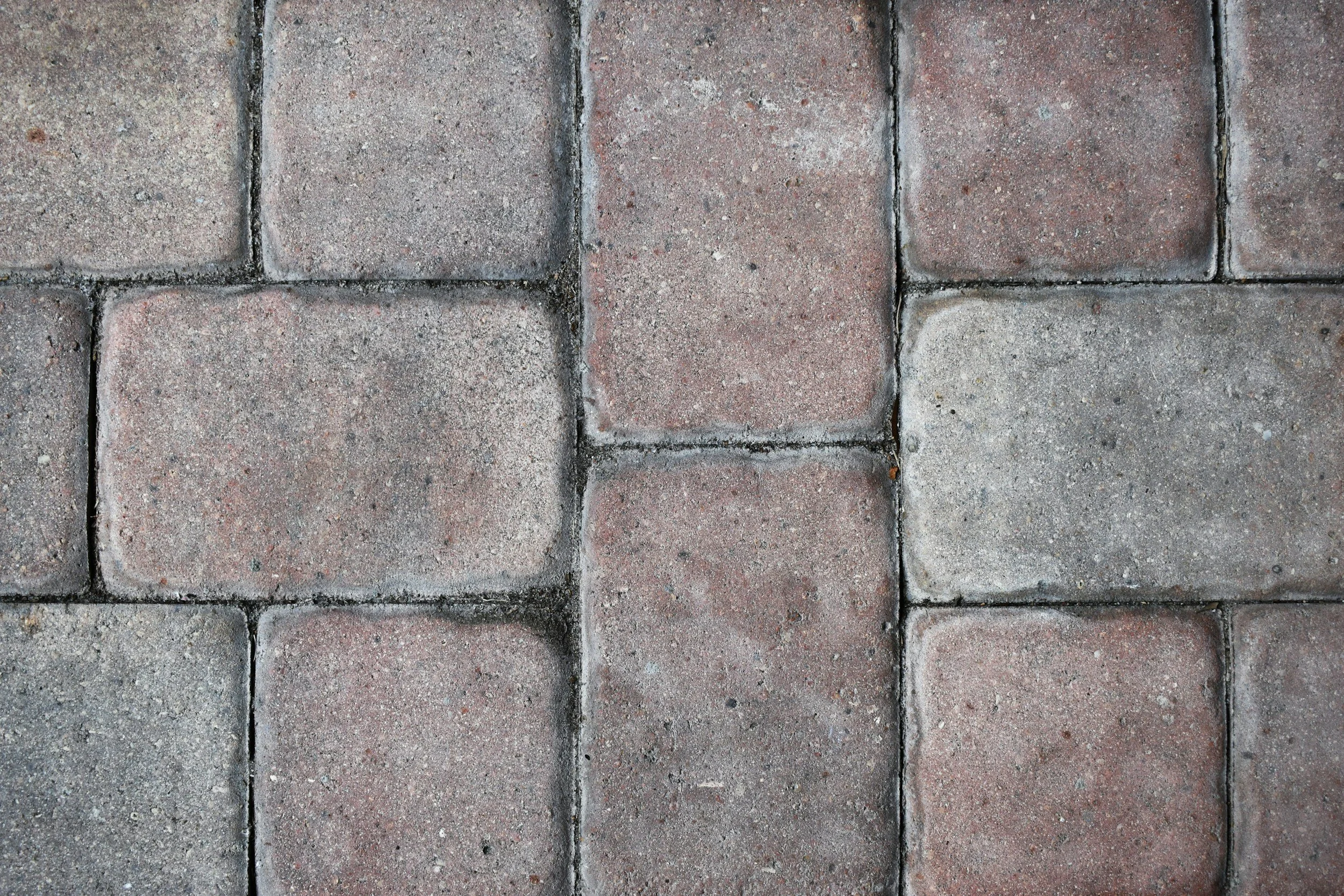 Close-up view of a brick pavement with rectangular bricks arranged in a grid pattern, showing various shades of red and gray.