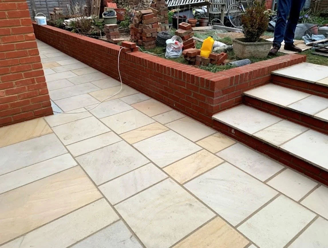 A newly built brick planter with tiles and stairs outside, surrounded by gardening materials and tools.