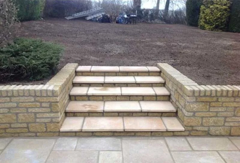 Brick steps leading up to a bare backyard with trees and shrubbery.