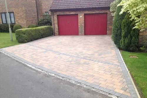 Paved driveway with red garage doors, bordered by grass and shrubs.