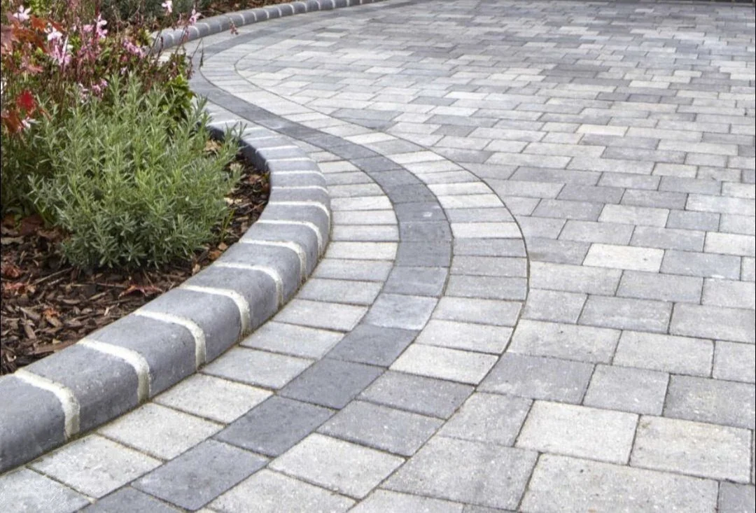 Close-up view of a brick pavement with rectangular bricks arranged in a grid pattern, showing various shades of red and gray.