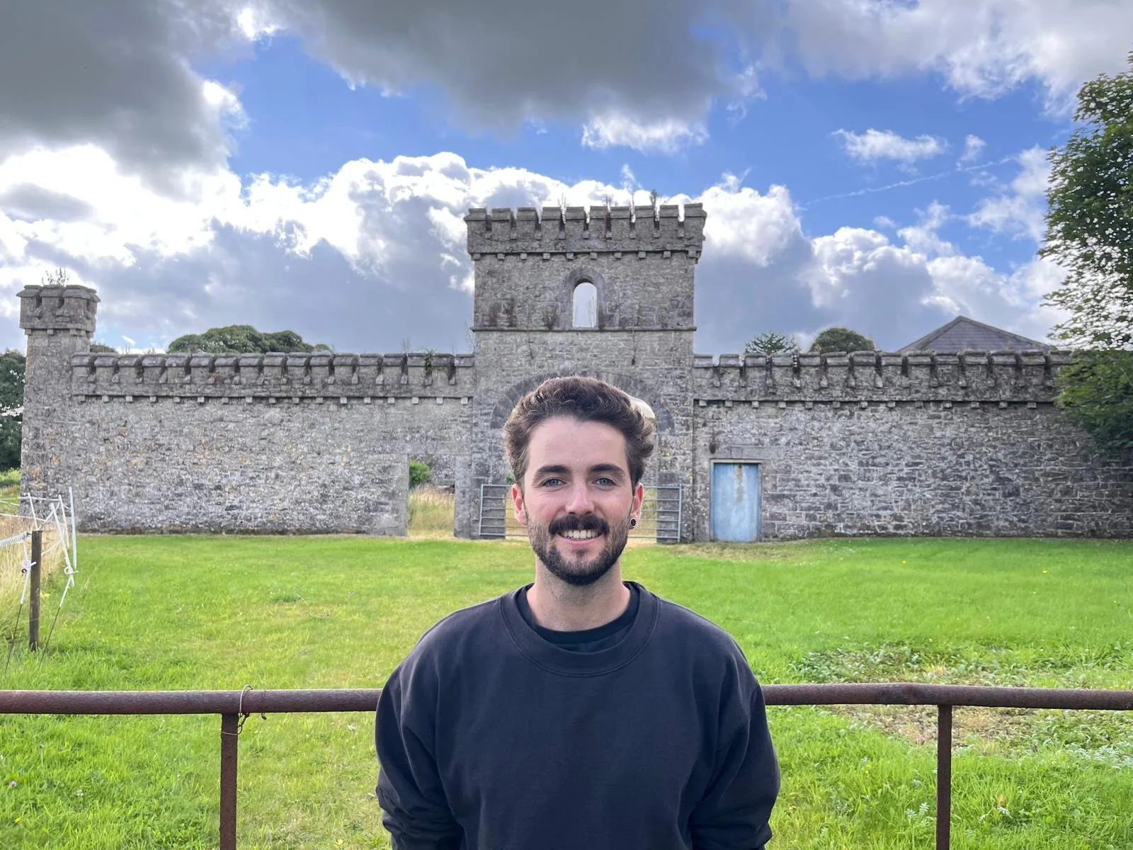 Junger Mann mit dunklem Pullover vor einer alten Steinburg
