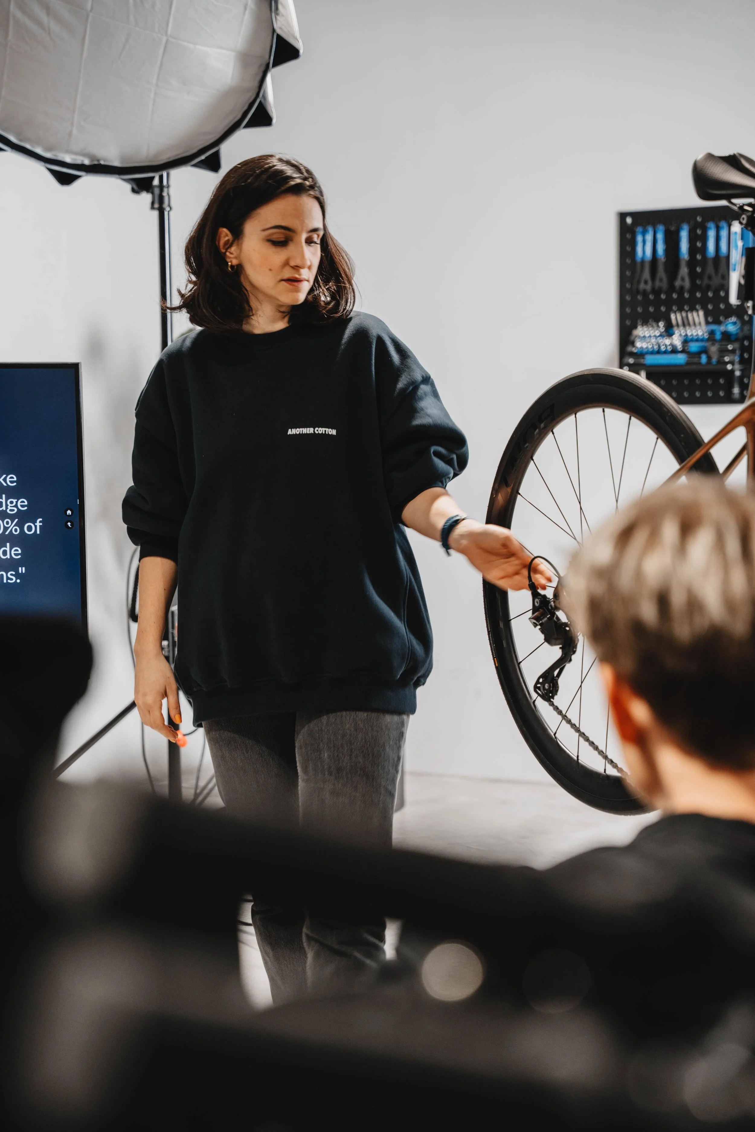 Eine Frau erklärt Kindern die Fahrradtechnik in einem Workshopraum, während sie neben einem Fahrrad steht.