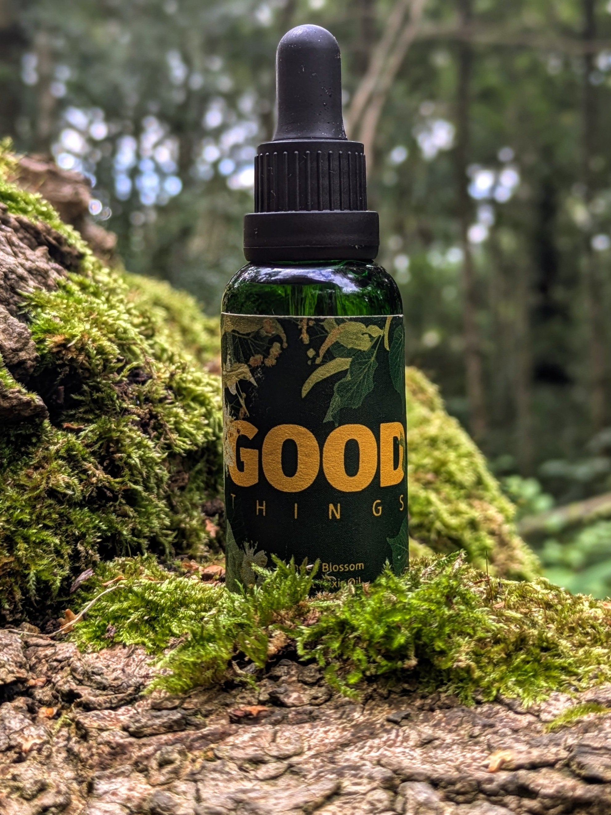 Glass bottle of Linden Blossom Night Elixir Oil with a golden dropper, surrounded by fresh linden flowers