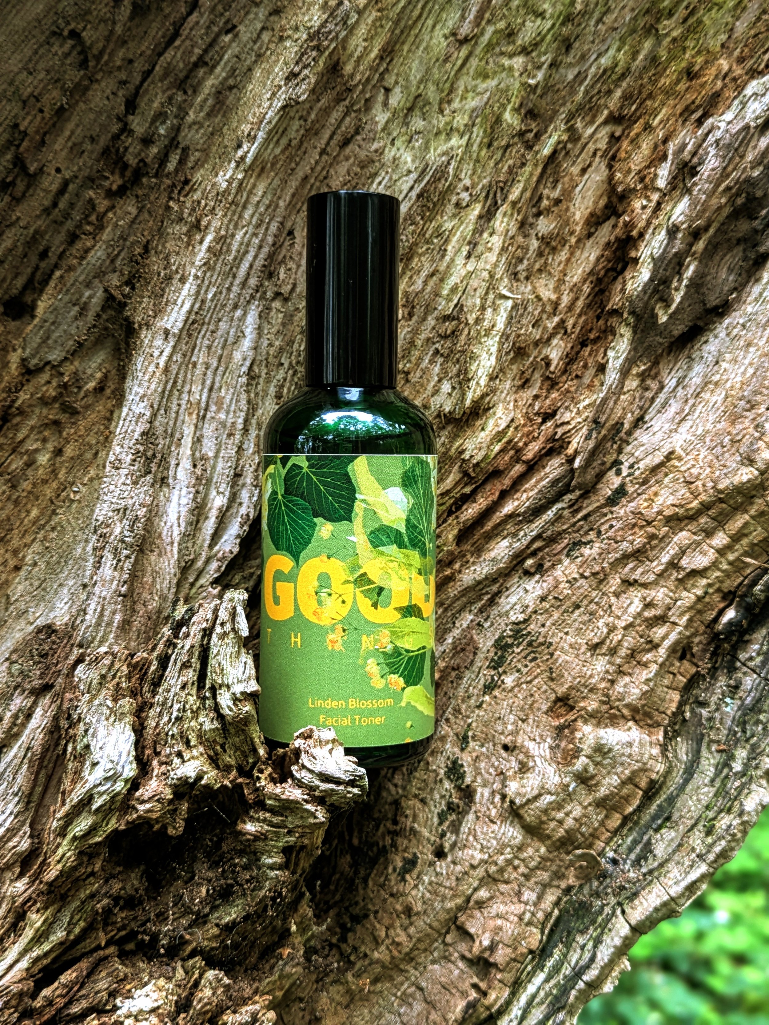 Amber spray bottle of Linden Blossom Facial Toner Mist placed beside fresh linden flowers on a wild tree background
