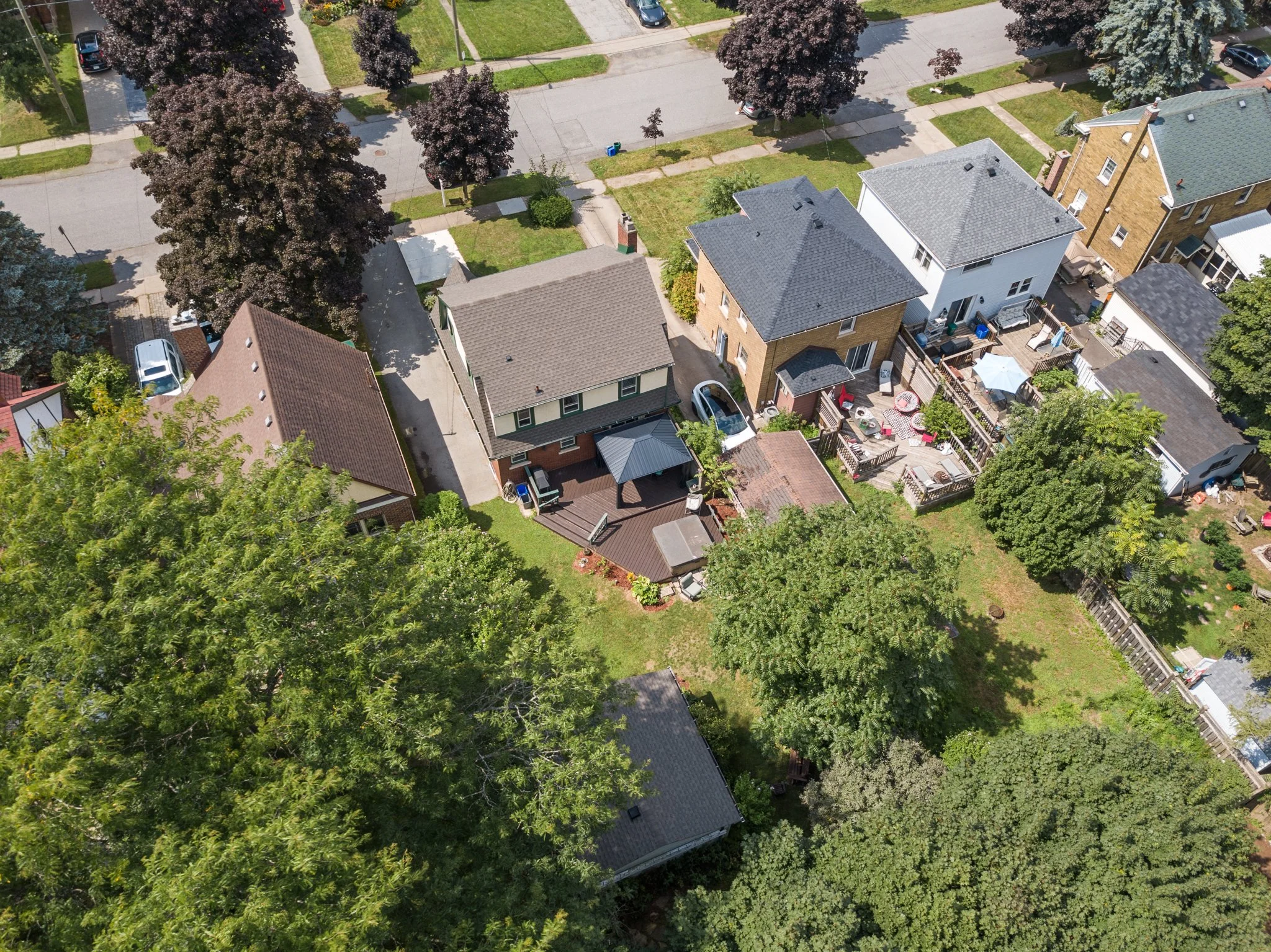 Aerial view of a residential neighborhood showing several houses with fenced backyards, trees, and a street with parked cars.