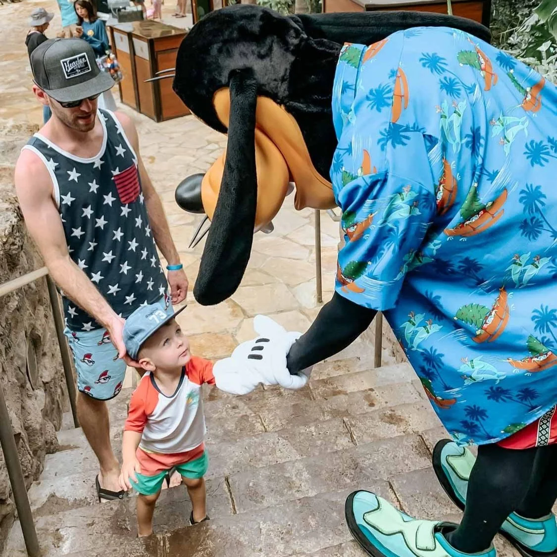 Little boy giving Disney character Goofy a high five while climbing stair at Aulani in Hawaii