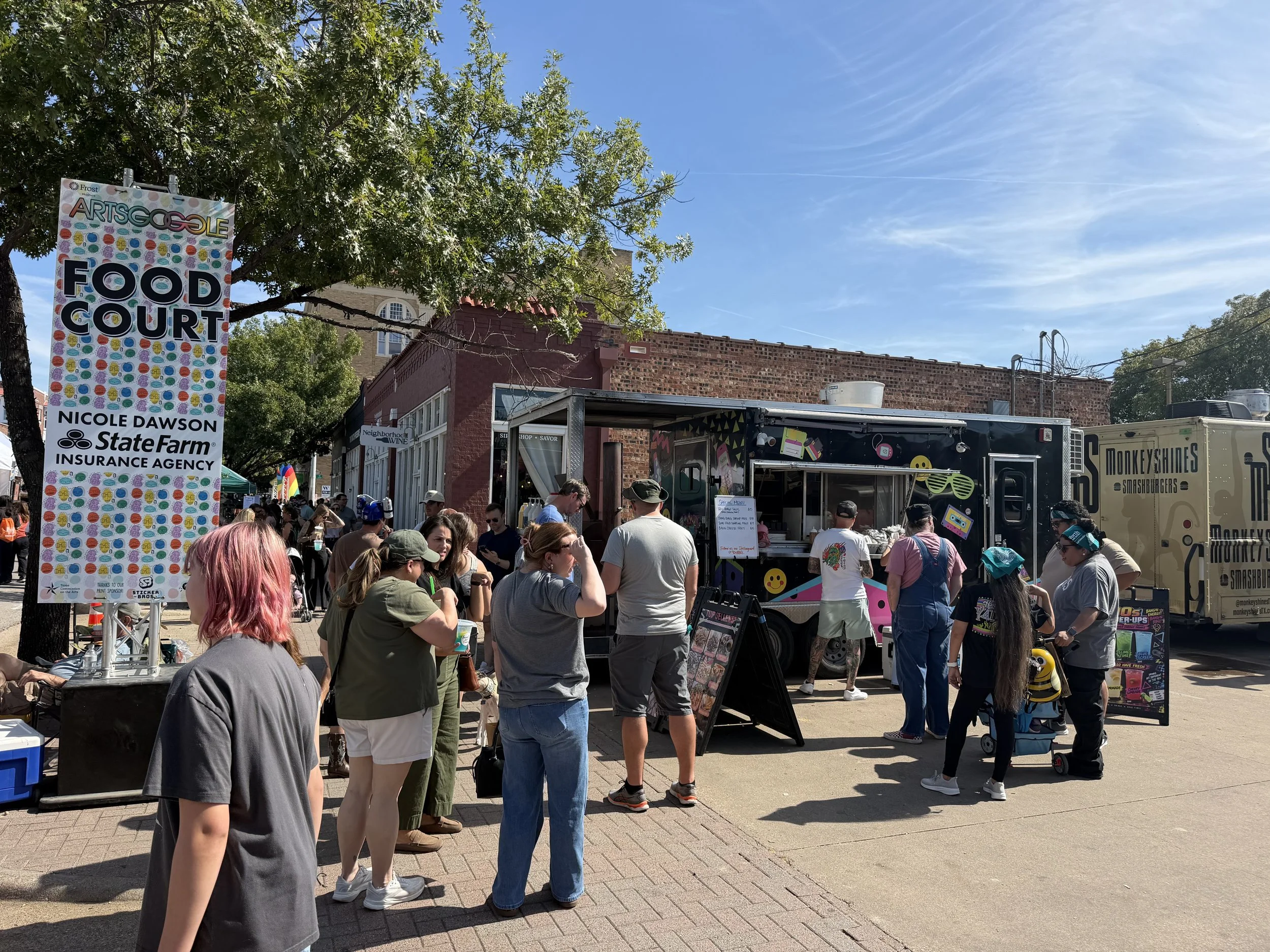 Crowded outdoor food court with colorful food trucks, festival booths, and an ArtsGoggle event sign.