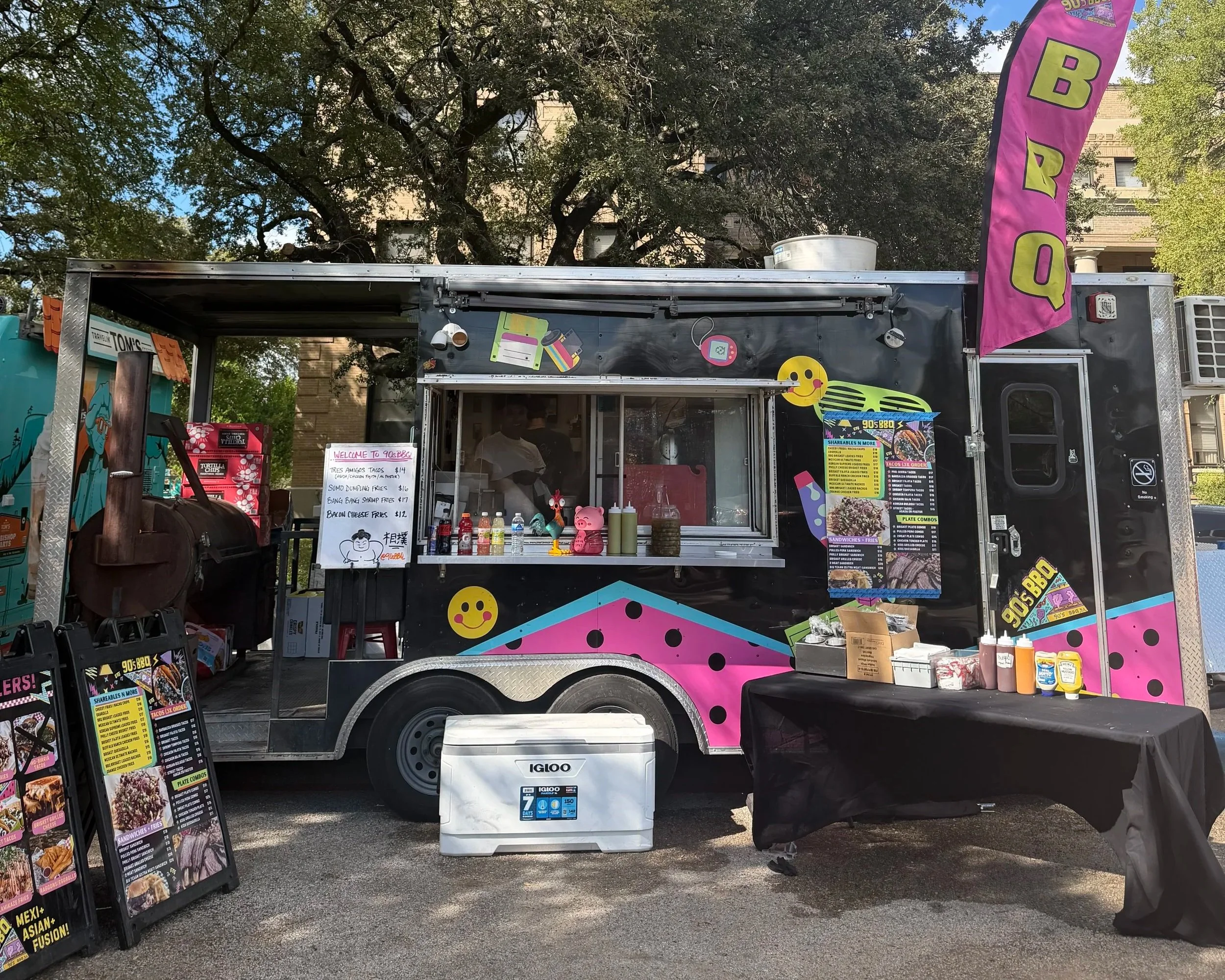 Colorful 90s BBQ food truck serving tacos, barbecue, fries, and sandwiches at an outdoor event.