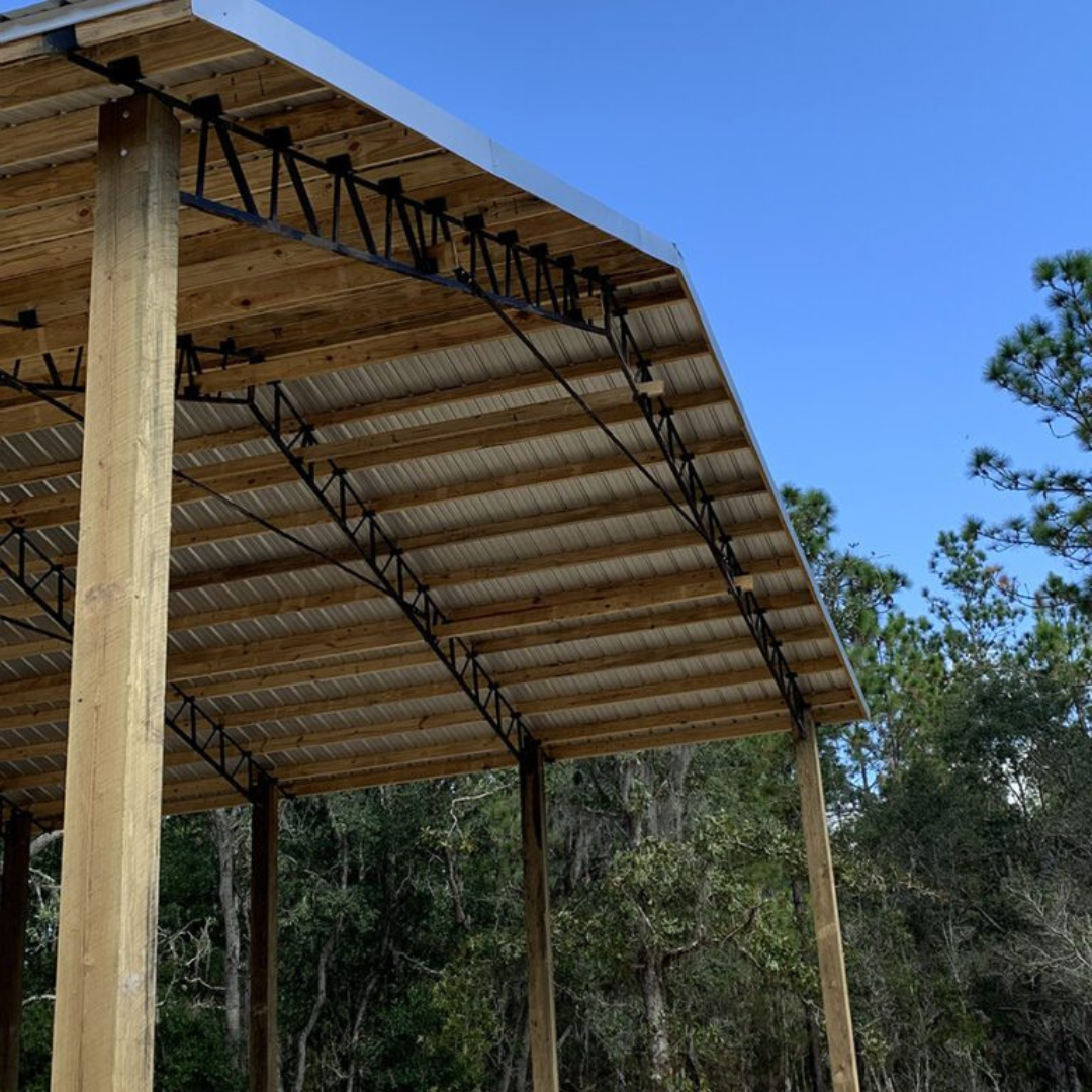 Pole Barn with wood beams, metal trusses, and metal roof with a clear blue sky and trees in the background.