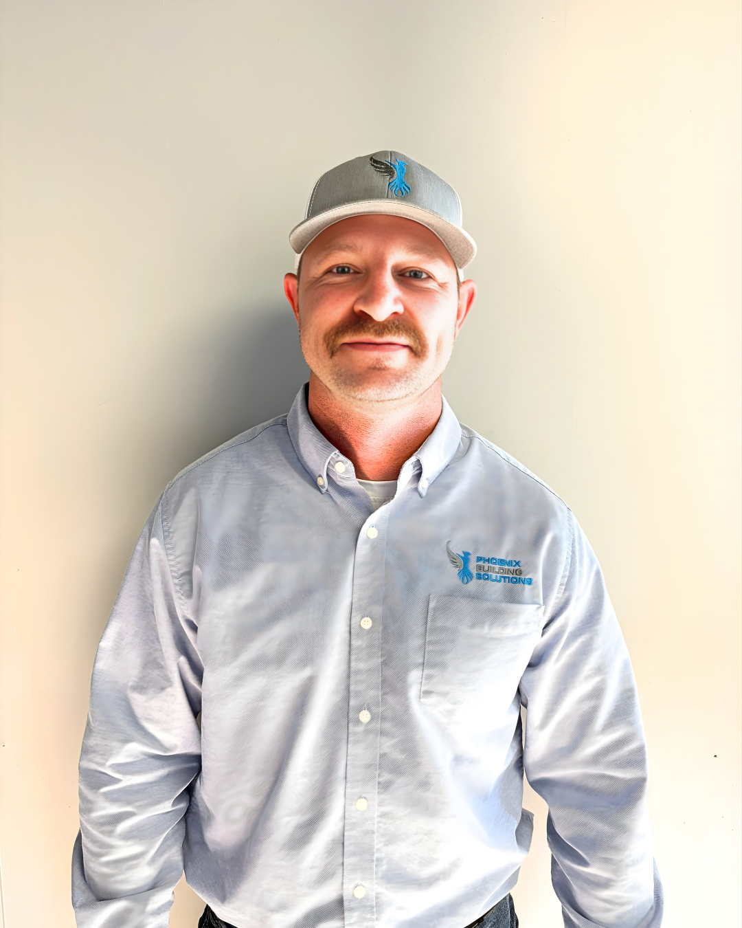 Professional headshot of Josh Kennedy, a Sales Representative for Phoenix Building Solutions, wearing a light blue button-down shirt with the company logo and a grey branded baseball cap against a neutral background. - Phoenix Building Solutions