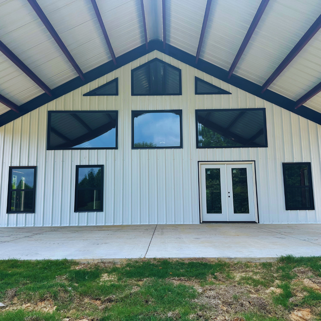 Close-up of a white metal building facade featuring a symmetrical arrangement of large black-framed windows and a central set of white double doors on a Barndominium by Phoenix Building Solutions. - Mississippi | Tupelo | Metal Buildings