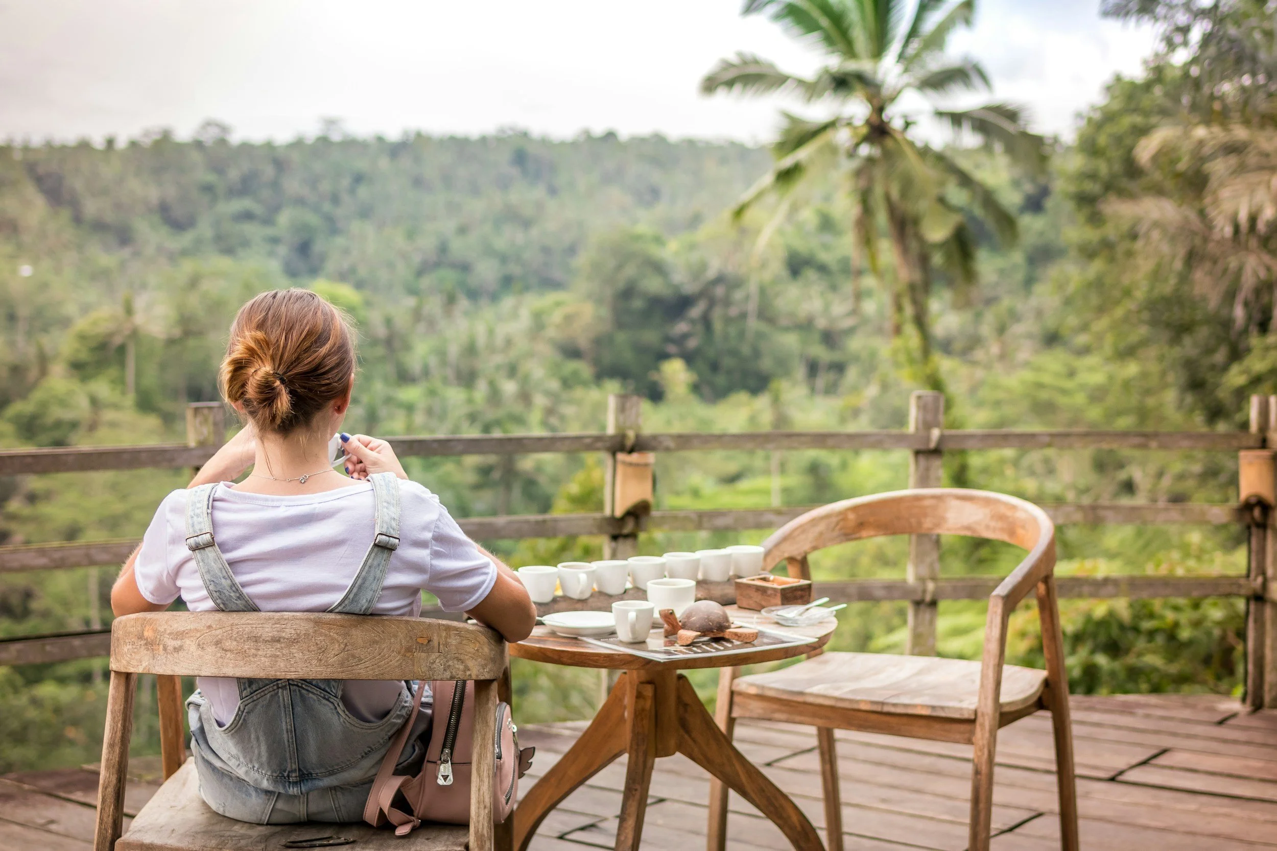 Woman sitting viewing a green tropical landscape drinking coffees.