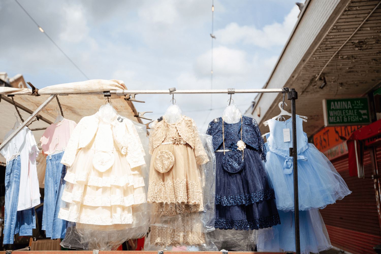 Multiple children's dresses for special occasions hanging from the rigging of a market stall in Newham