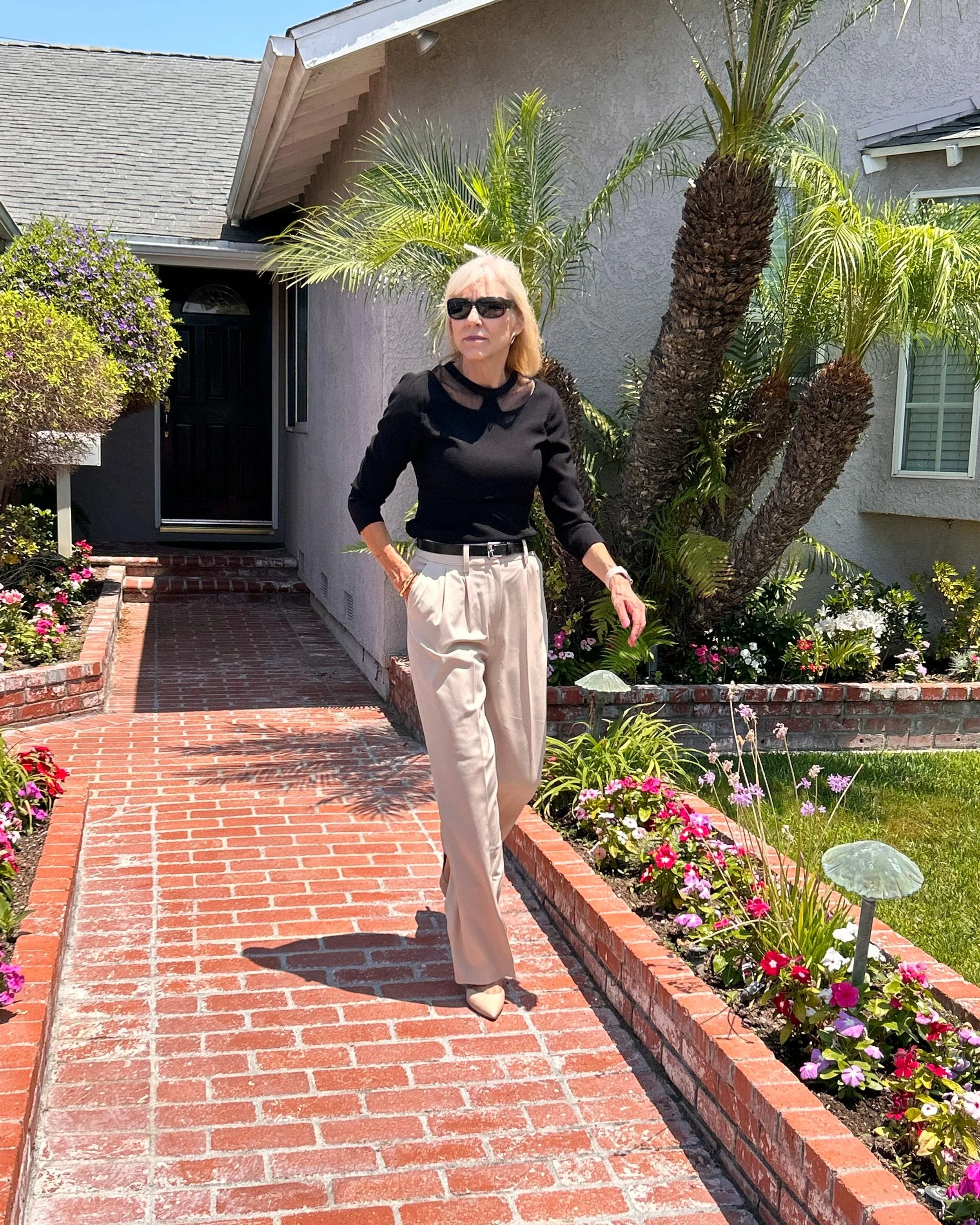 Colors other than black are ok for a summer funeral, Jacki wears taupe pants with a black blouse and taupe shoes for a modern summer funeral look