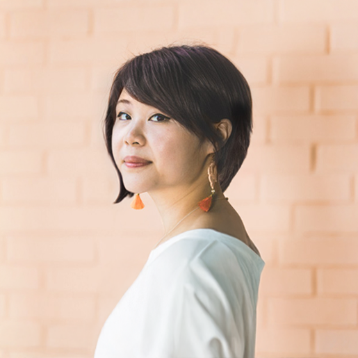 Close-up of a woman with short black hair, wearing orange earrings, and showing a colorful tattoo on her shoulder.
