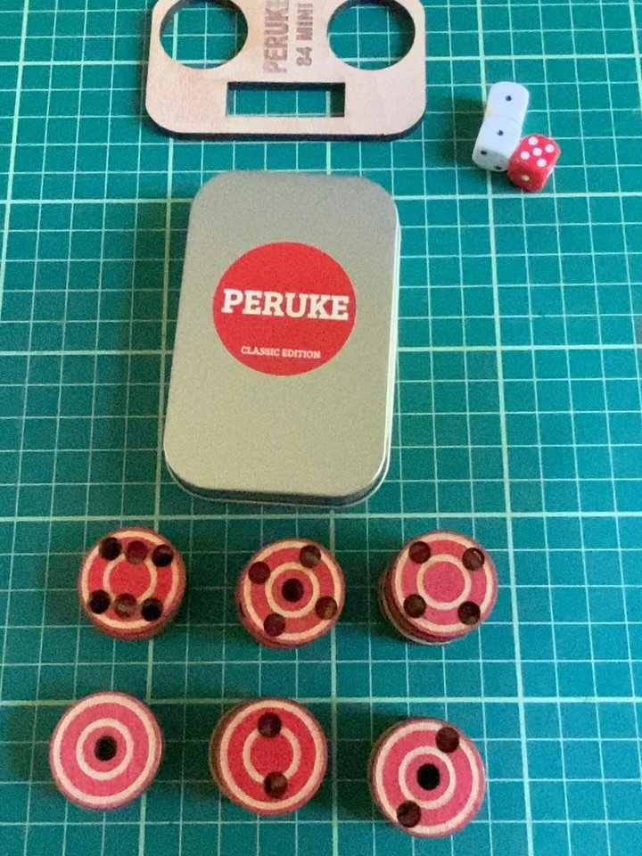 Peruke 84 mini edition. Same great board game but now perfect to take with you when you&rsquo;re out &amp; about. The 24 mini discs &amp; dice are housed perfectly in a little mint style tin. Combined with a lovely Cherry wood board these will be ava