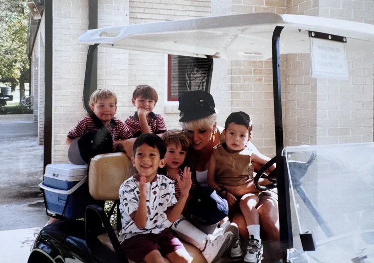 Young children and a counsellor packed into a golf cart outside a camp building