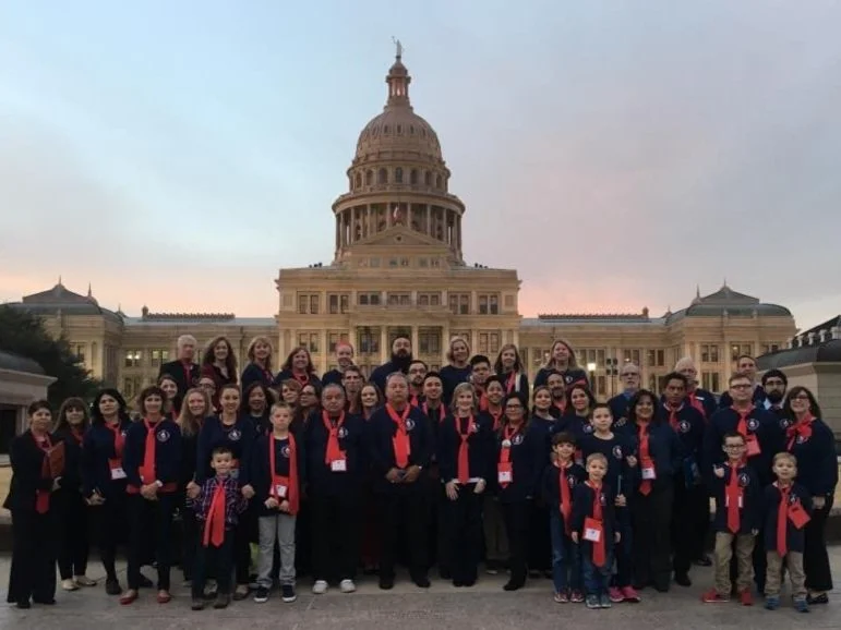 Texas advocates in navy and red gathered on the south steps of the Texas Capitol at dusk