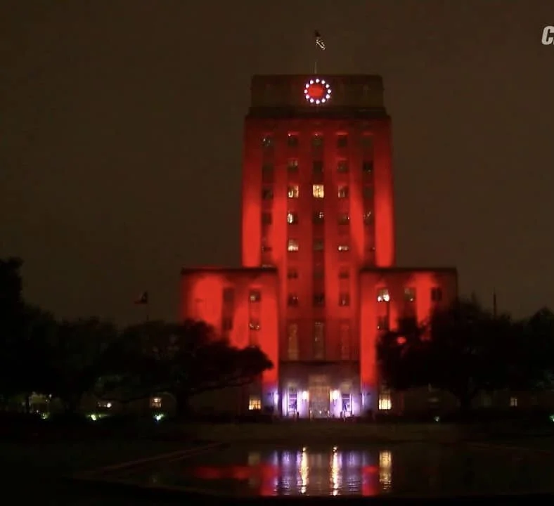 Houston City Hall lit red at night for Bleeding Disorders Awareness Month, reflected in the pool in front of it