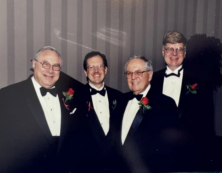 Four men in black tie with red rose boutonnieres at a chapter gala